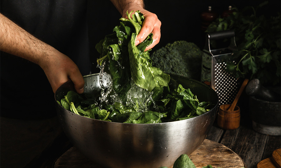 Hands of chef washing and mixing fresh homemade spinach leaves on wooden desk.
