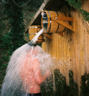 Young man pours a bucket of cold water on himself in sauna