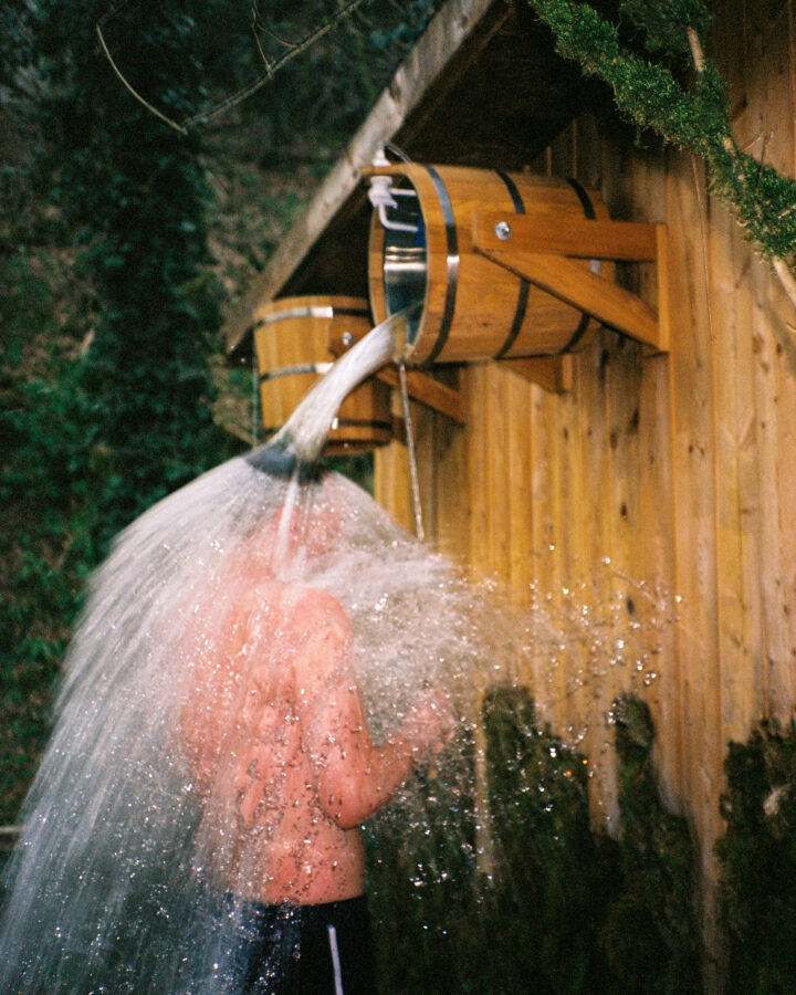 Young man pours a bucket of cold water on himself in sauna