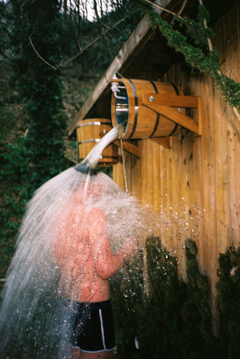 Young man pours a bucket of cold water on himself in sauna