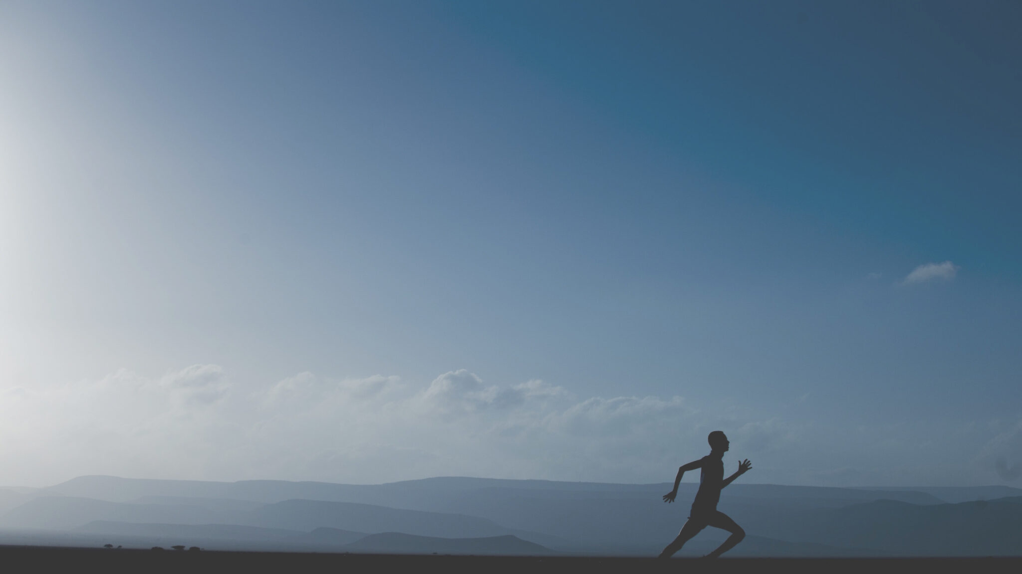 Lone runner silhouetted against a wide sky above the sea