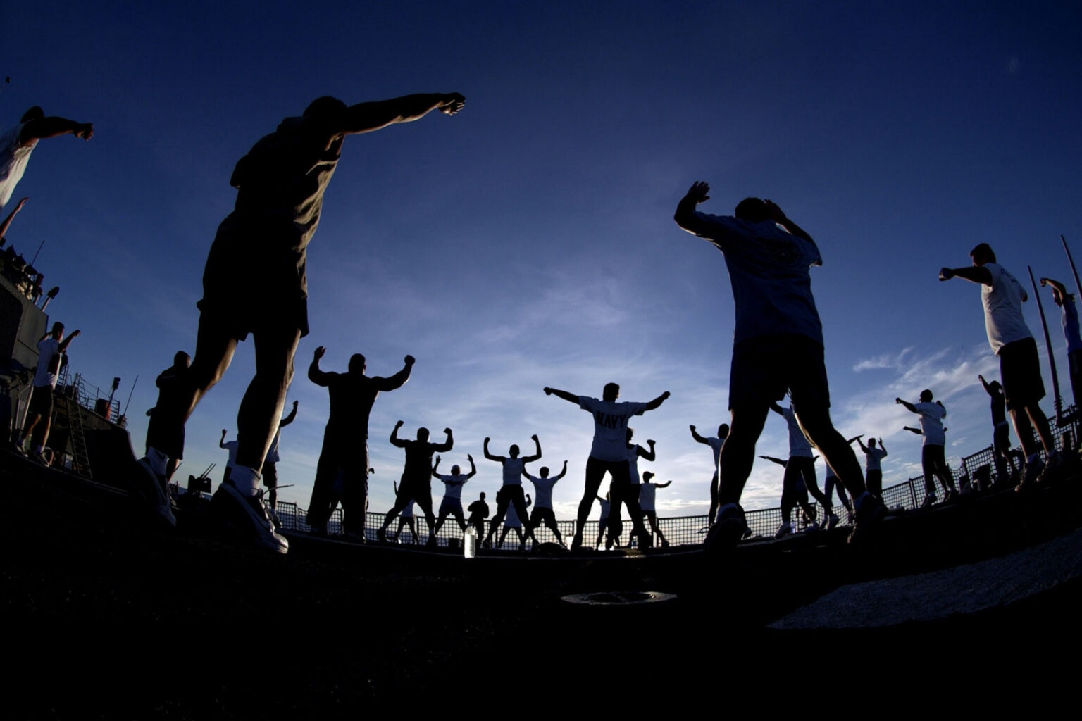 Group exercising outdoors, silhouetted against an evening sky