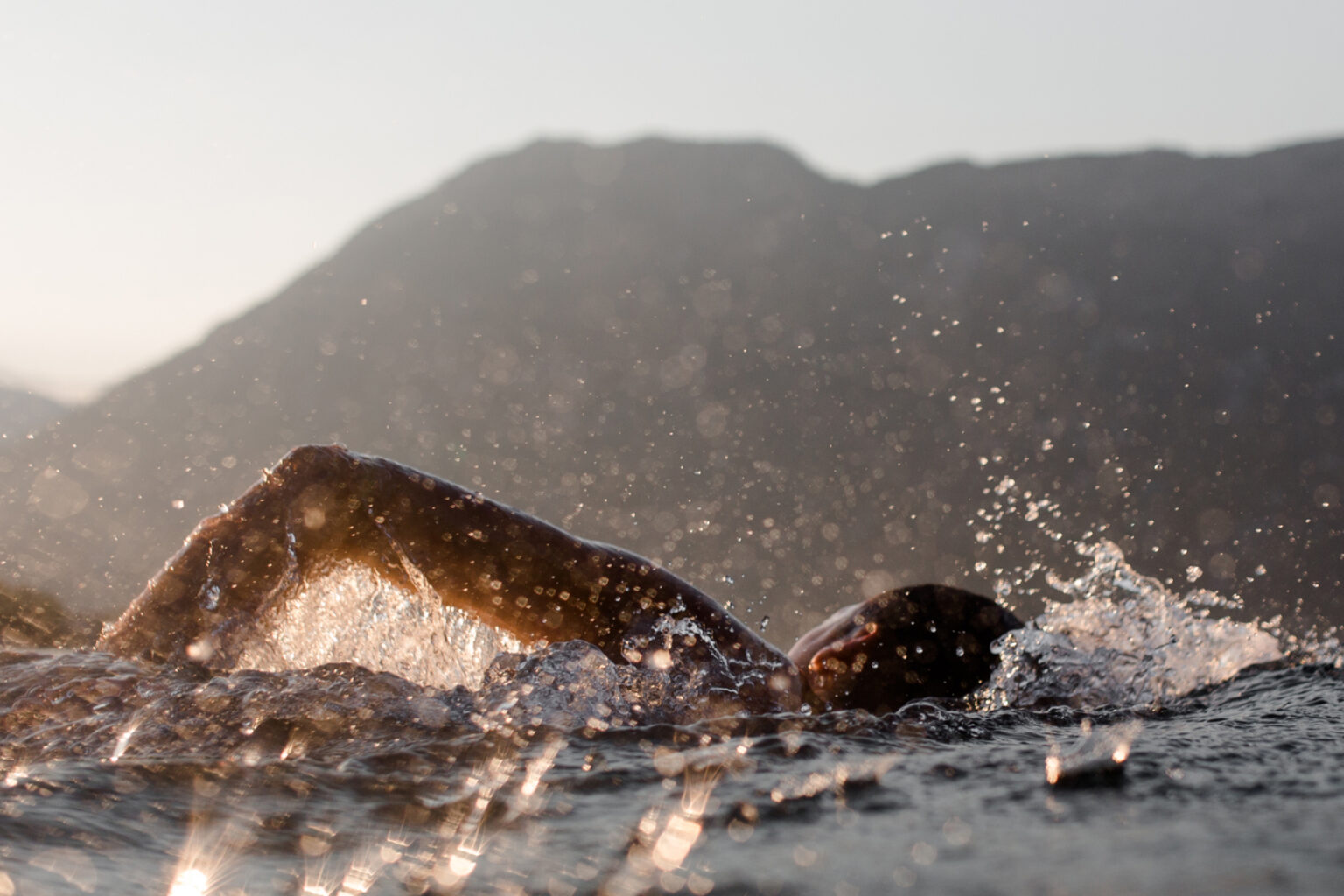 Open-water swimmer mid-stroke beneath mountains